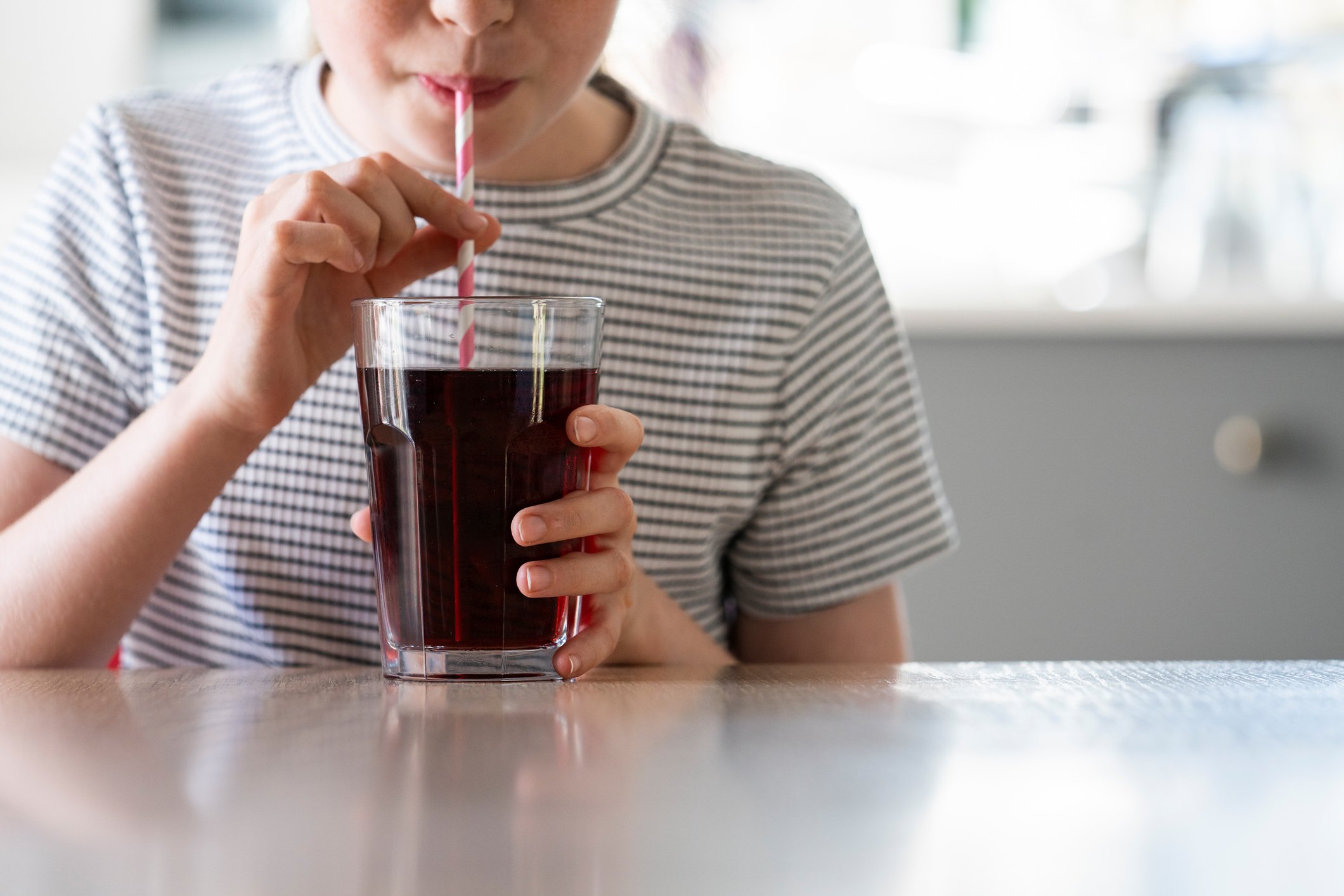 Person drinking from a glass of cola with a straw.