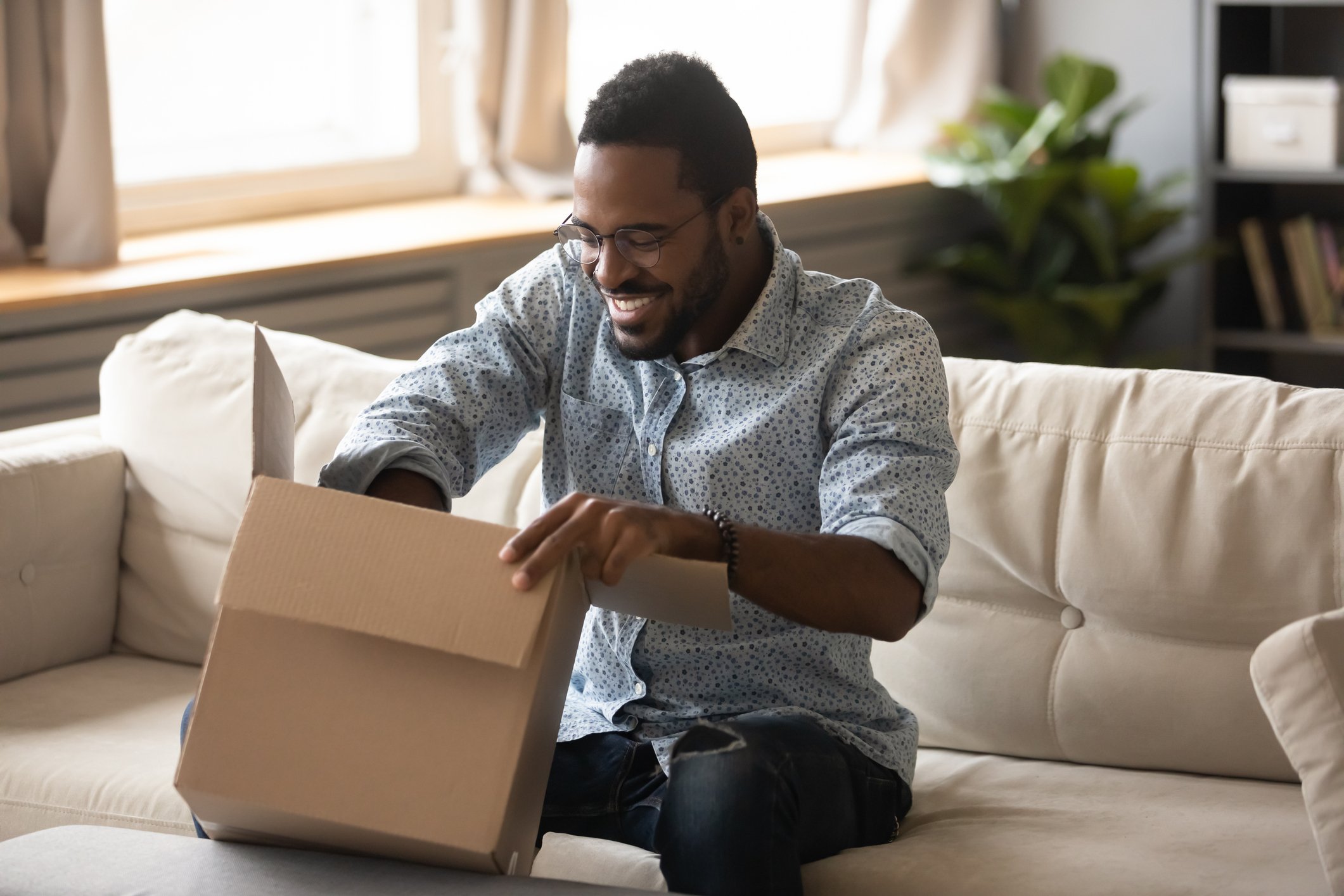 A young man eagerly opens a cardboard package in his living room. 
