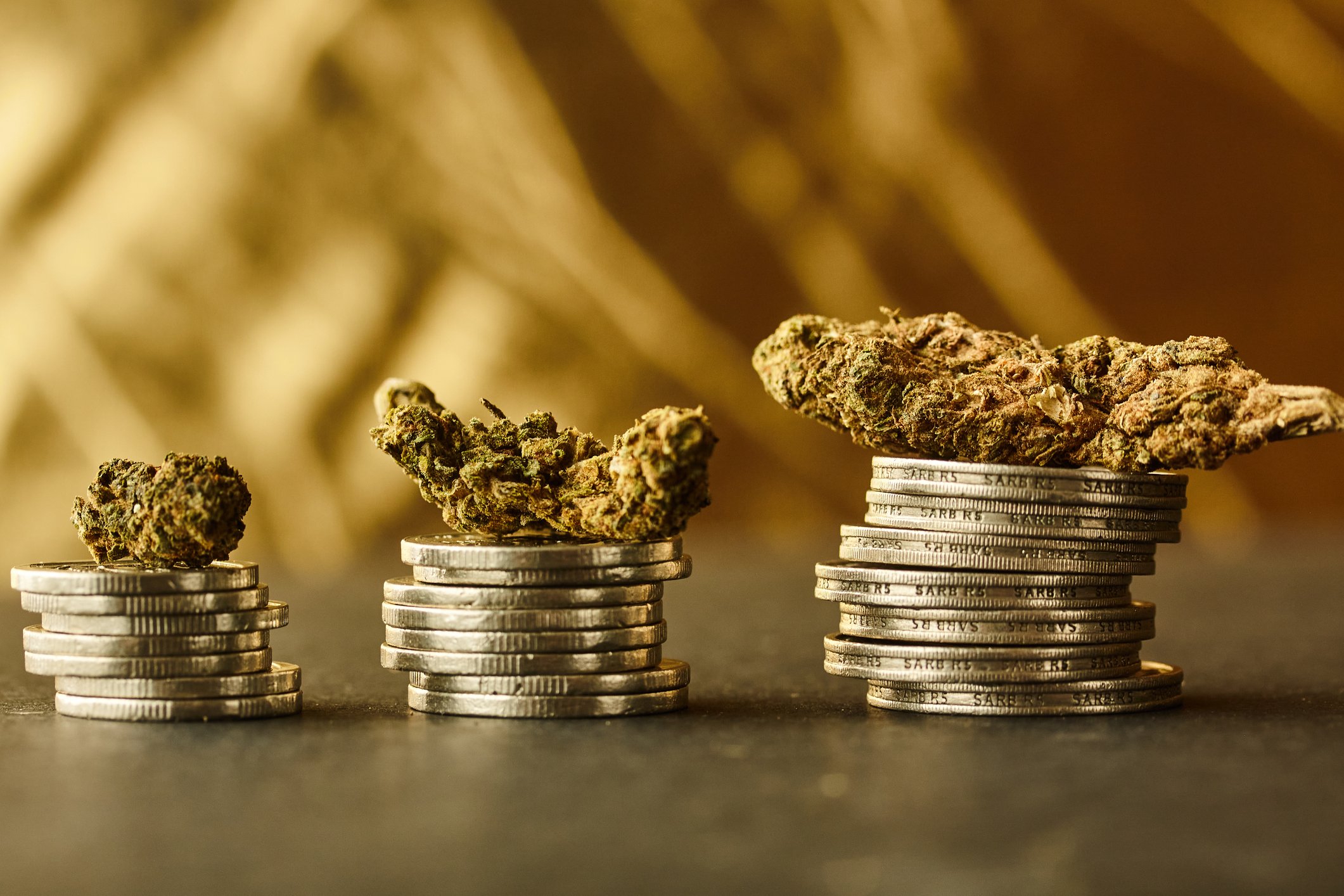 Three ascending stacks of coins each with a marijuana bud on top of it. 