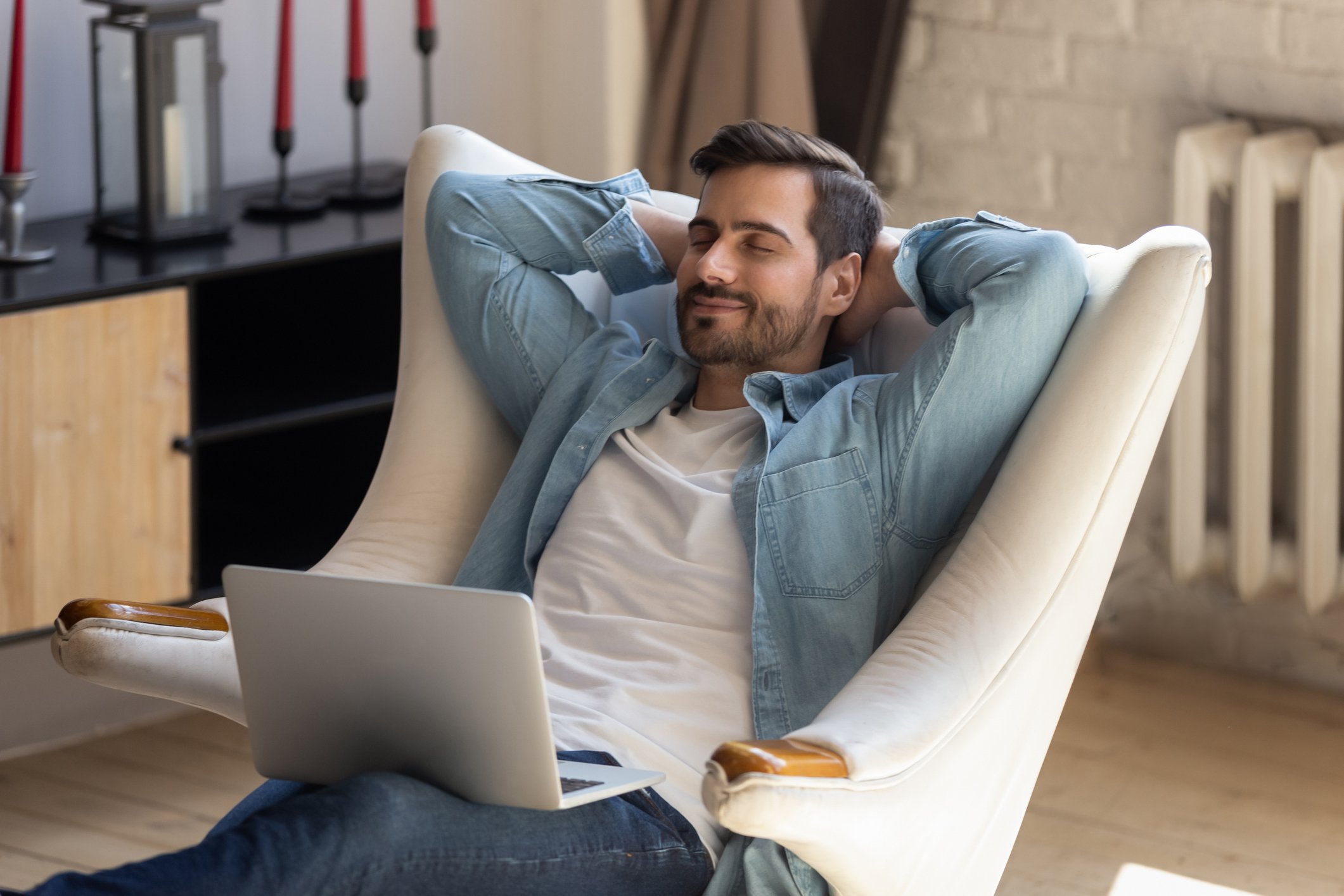 A man relaxing in a padded white lounge chair with a laptop on his lap.