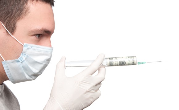 Man wearing a mask holding a syringe with cash inside it