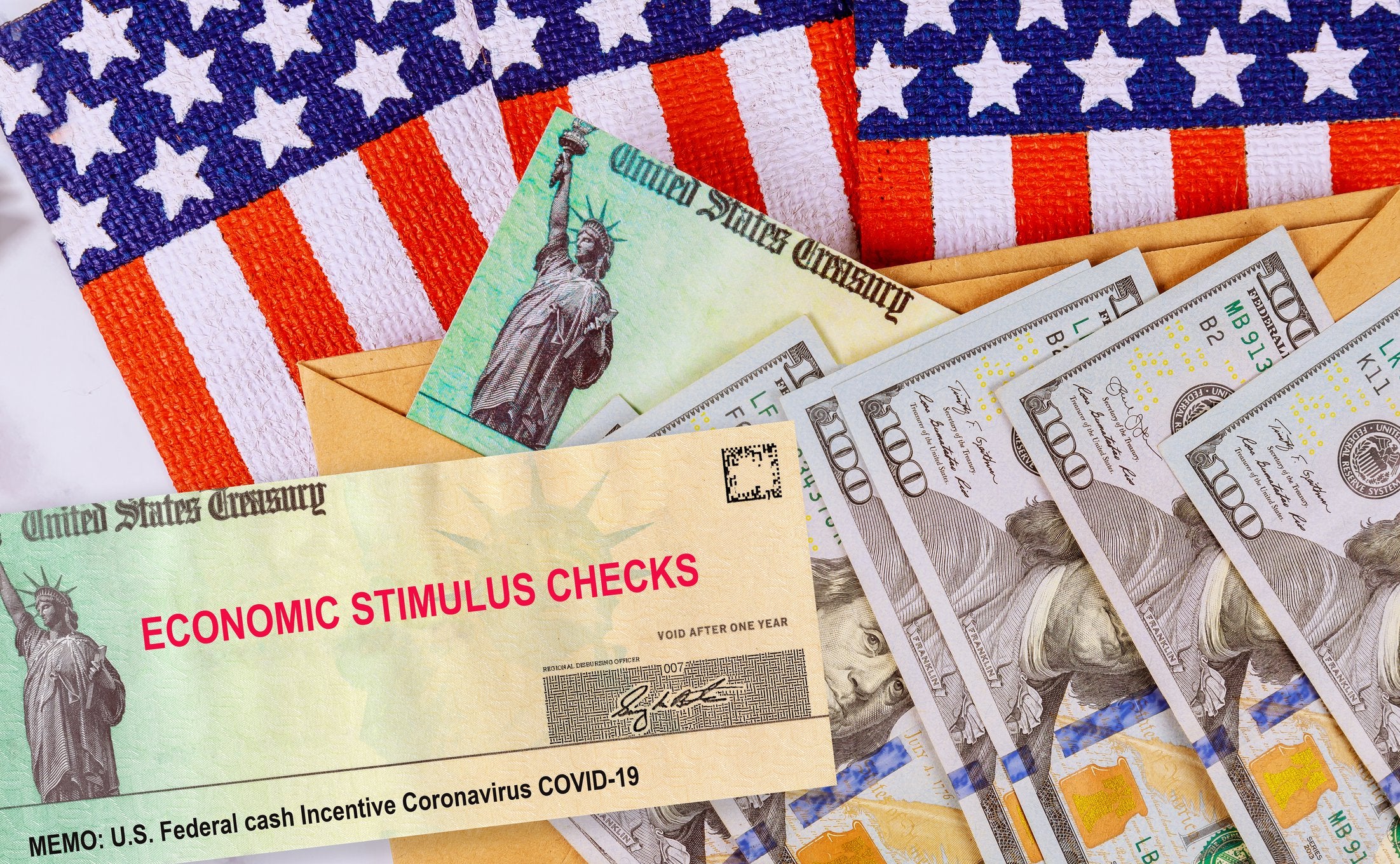 Economic stimulus check and hundred dollar bills atop American flags.