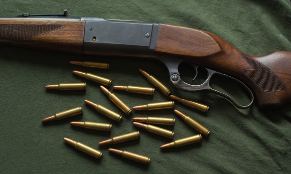 A lever-action rifle with a checkered stock and buckhorn sights, lying on a green cloth with brass-cased ammunition.