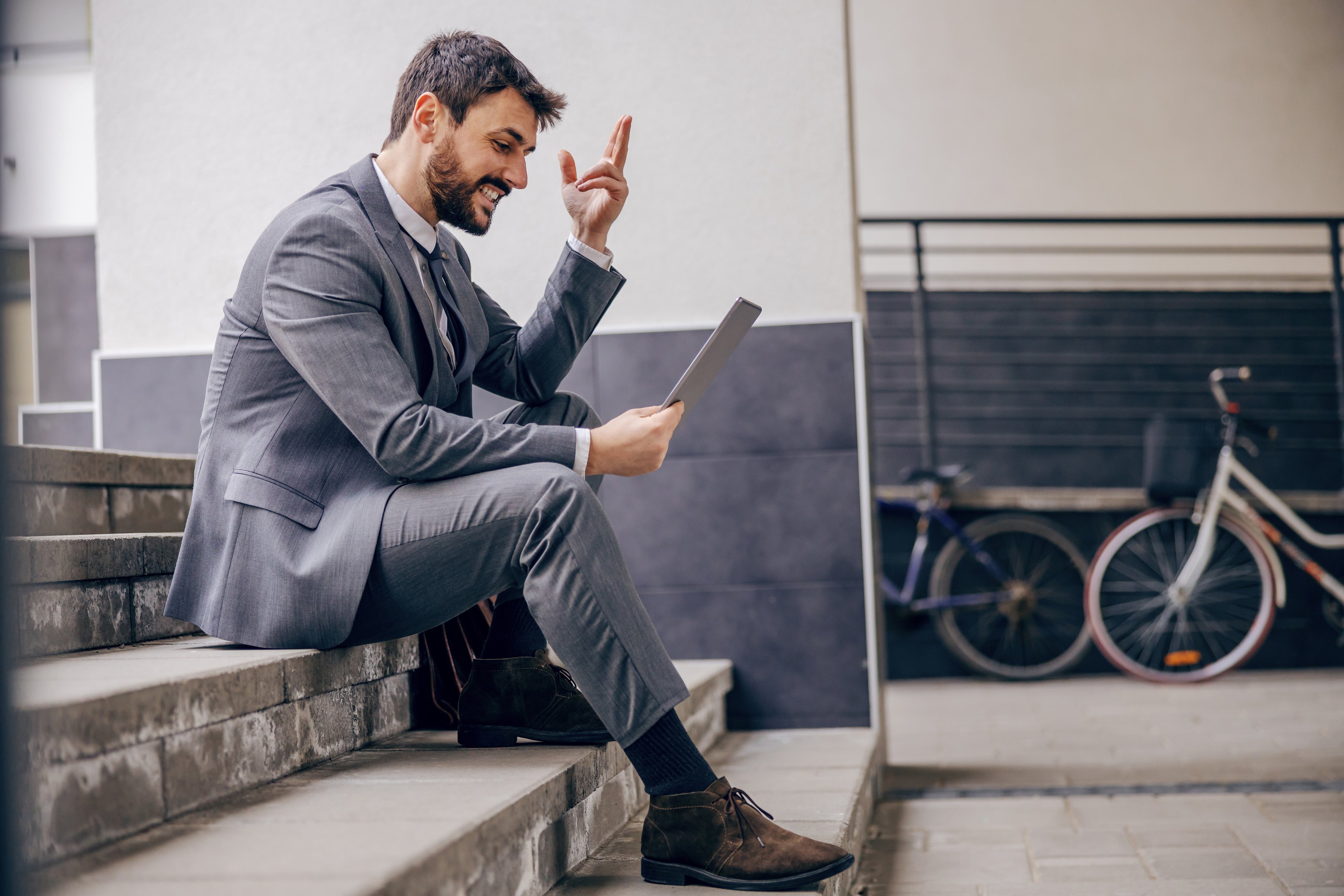Man in grey suit sits on stone steps, holding an iPad. A mirror reflecting a bicycle sits in background.