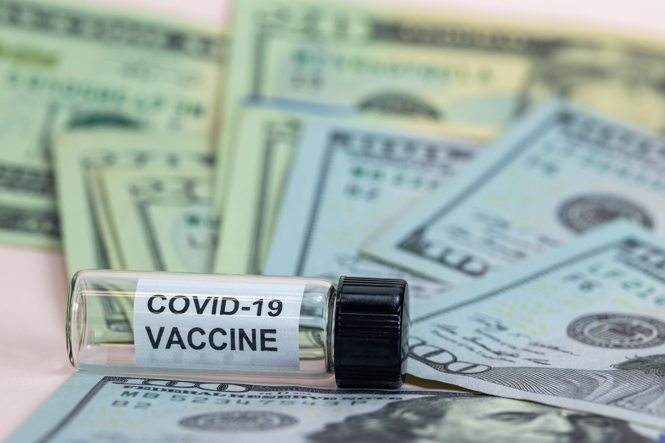 A vial of COVID-19 vaccine resting on a bed of $100 bills.