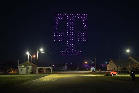 Drones with magenta lights forming the T-Mobile logo in the sky.