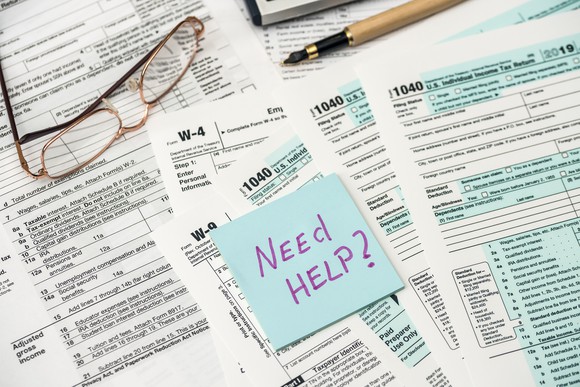 A pile of tax forms with a Post-it note asking "Need Help?"