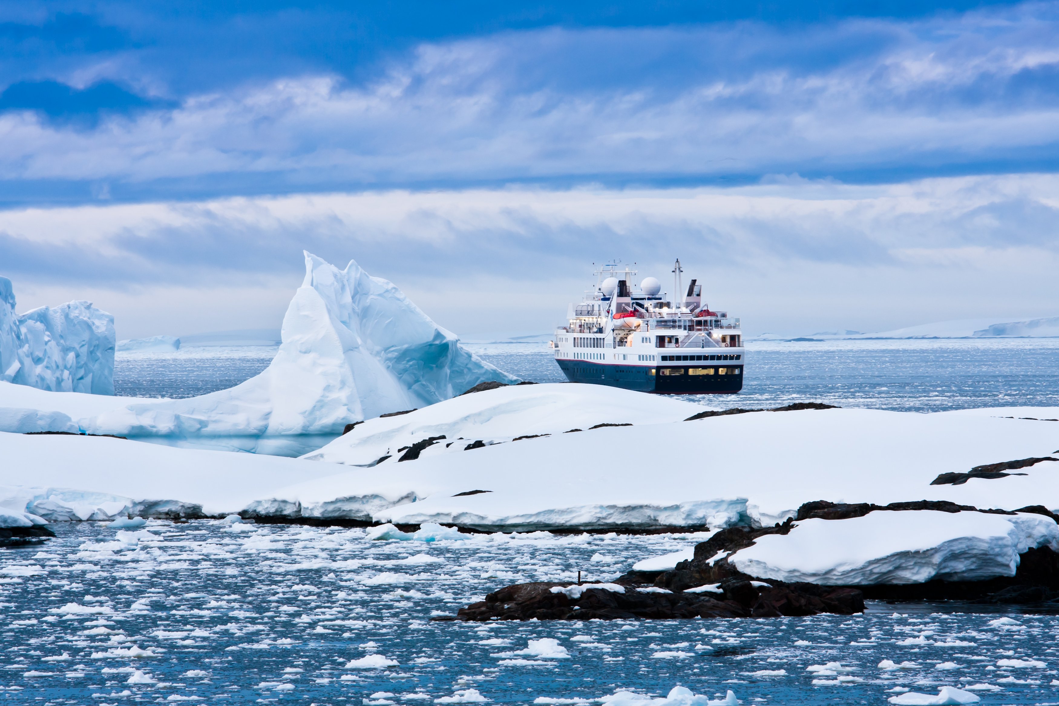 A cruise ship sails next to a glacier and ice cap in polar waters. 