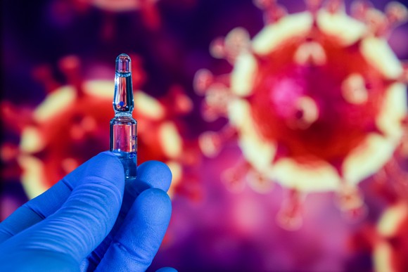 Gloved hand holding up a vial in front of images of the coronavirus