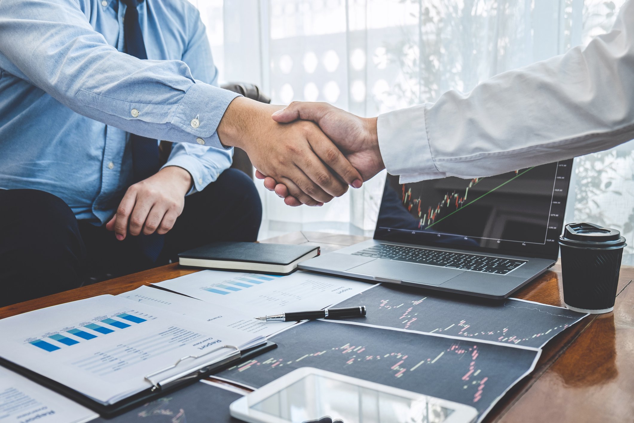 Two businesspeople shaking hands over a desk in an office.