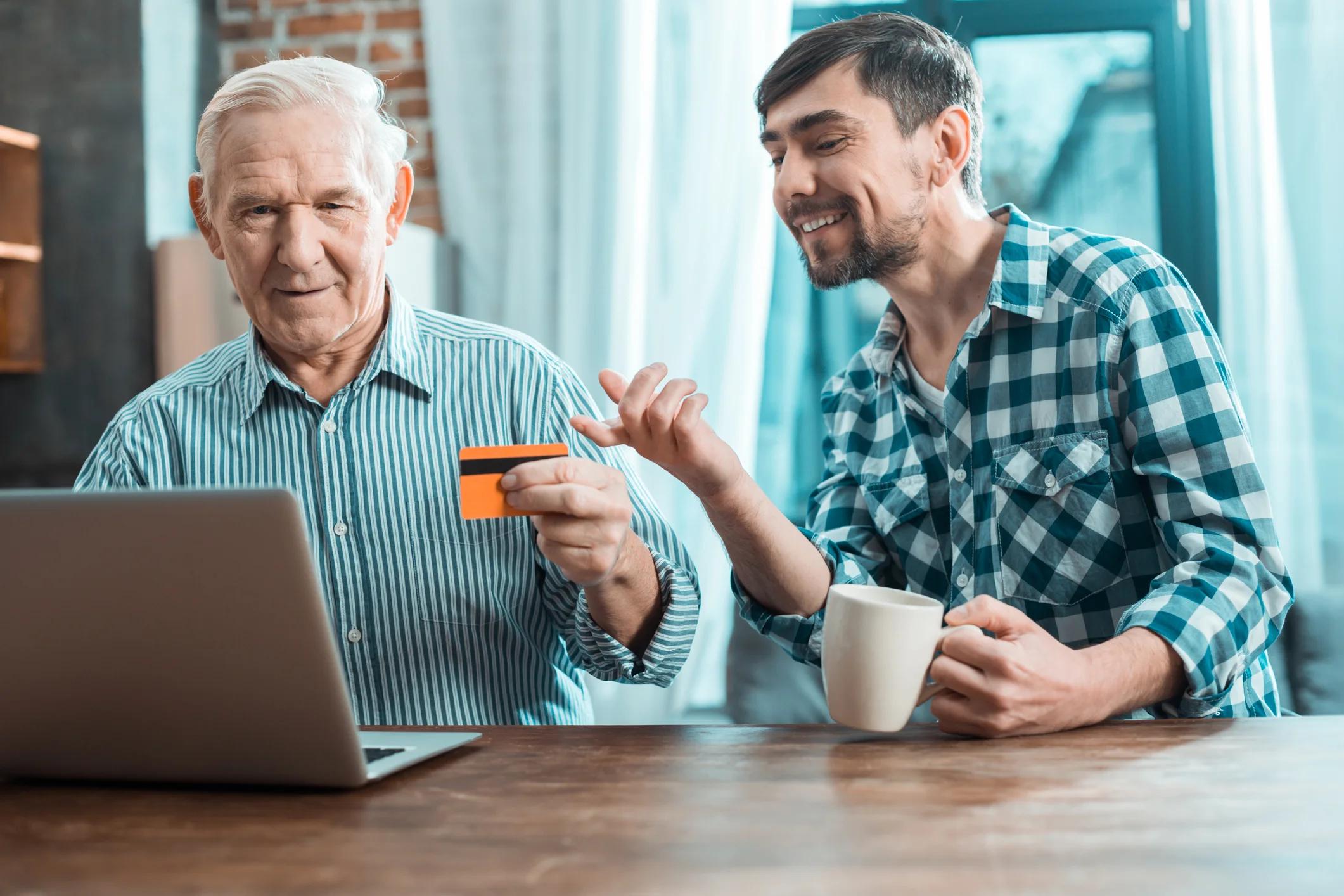 Older person holding credit card with younger person pointing at screen.