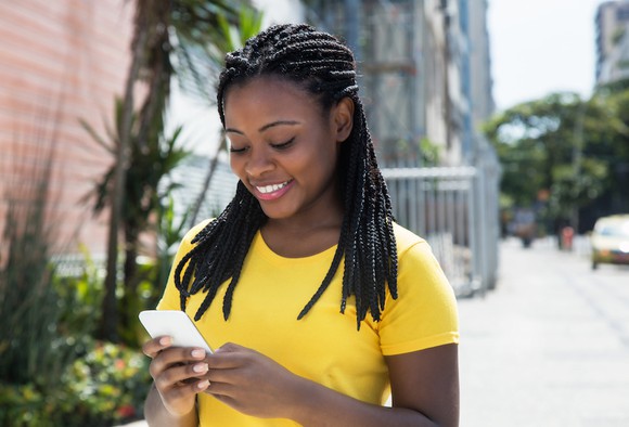 A woman smiles while looking at a smartphone.