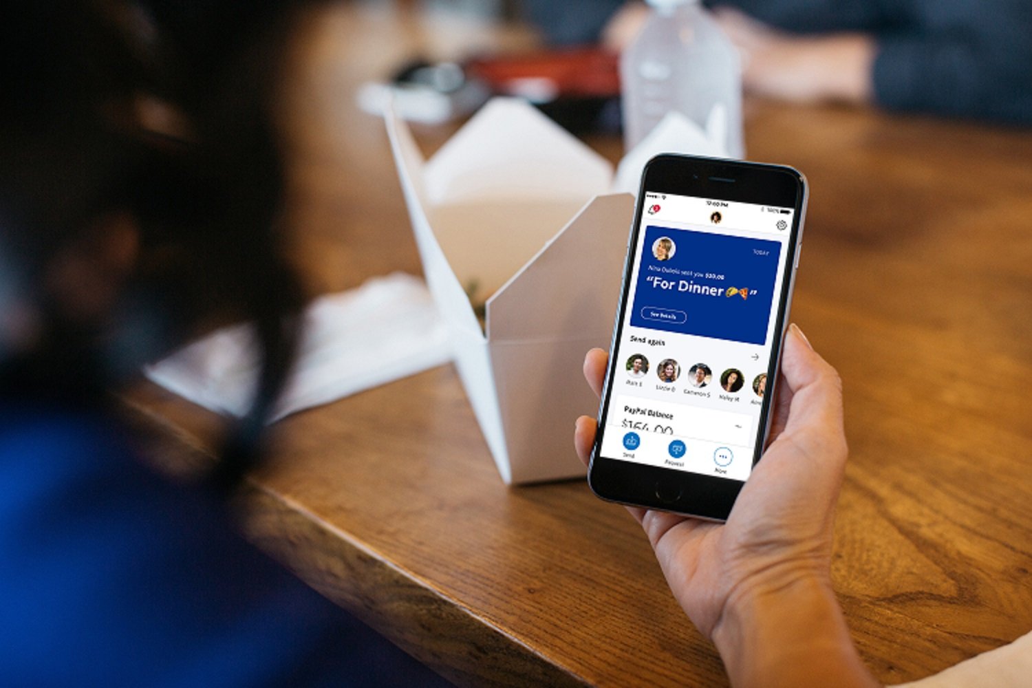 A smartphone displays the PayPal app in a restaurant setting.