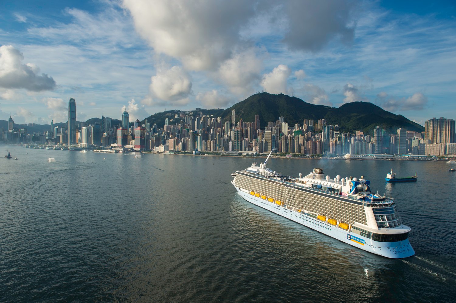 Royal Caribbean's Quantum of the Seas sailing off Hong Kong under a cumulus-dotted sky.