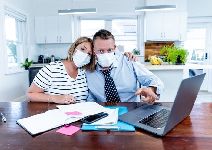 Masked couple sitting at table with laptop, calculator, and documents.