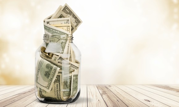 A mason jar full of folded U.S. currency on a table.