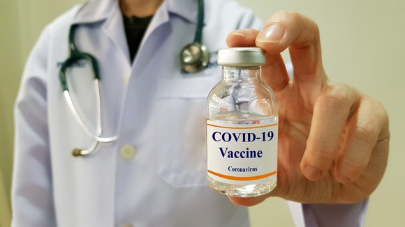 A doctor holding a vial labeled "COVID-19 Vaccine"