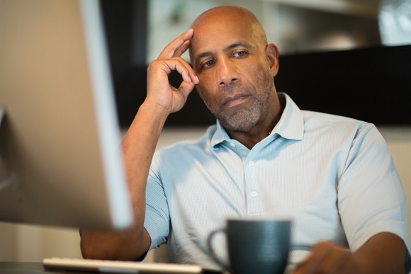 Older man sitting in front of monitor, thinking.