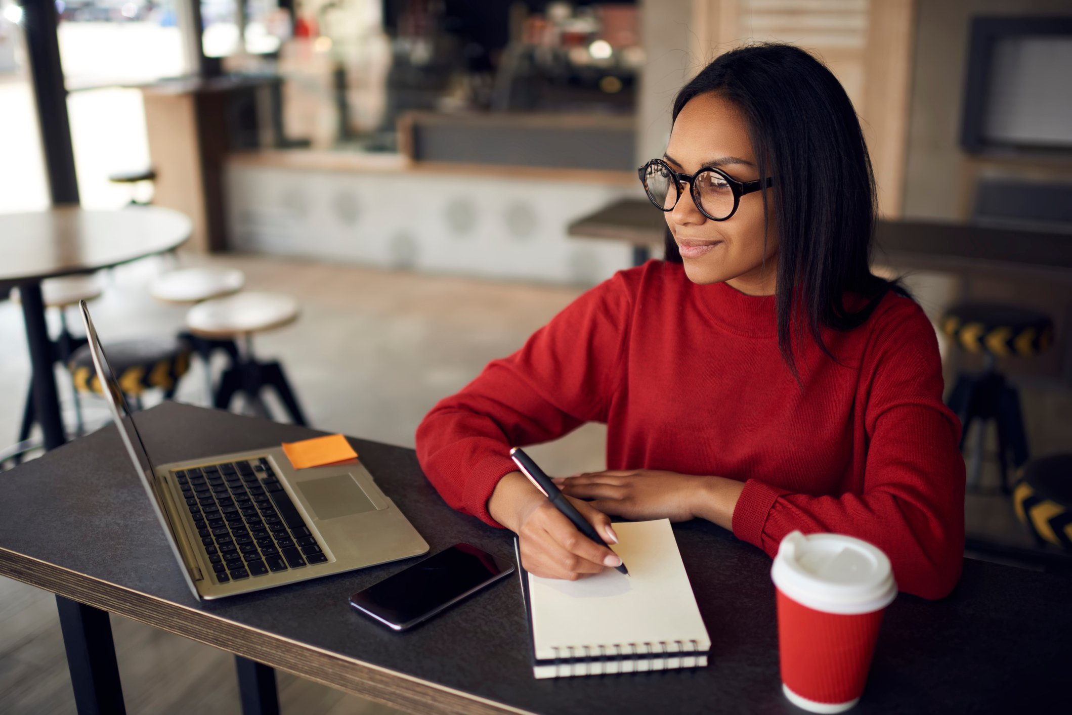 Woman looking at laptop and taking notes in coffee shop