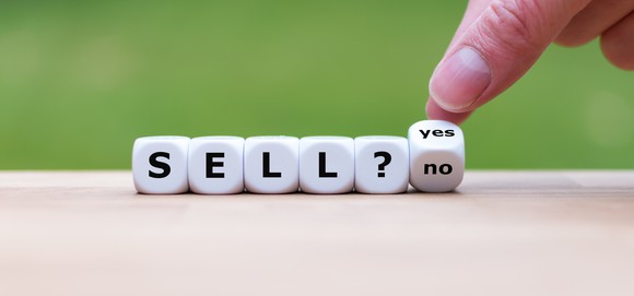 Die spelling "Sell?" with a person's fingers holding another dice at an angle to display "yes' on one side and "no" on another side