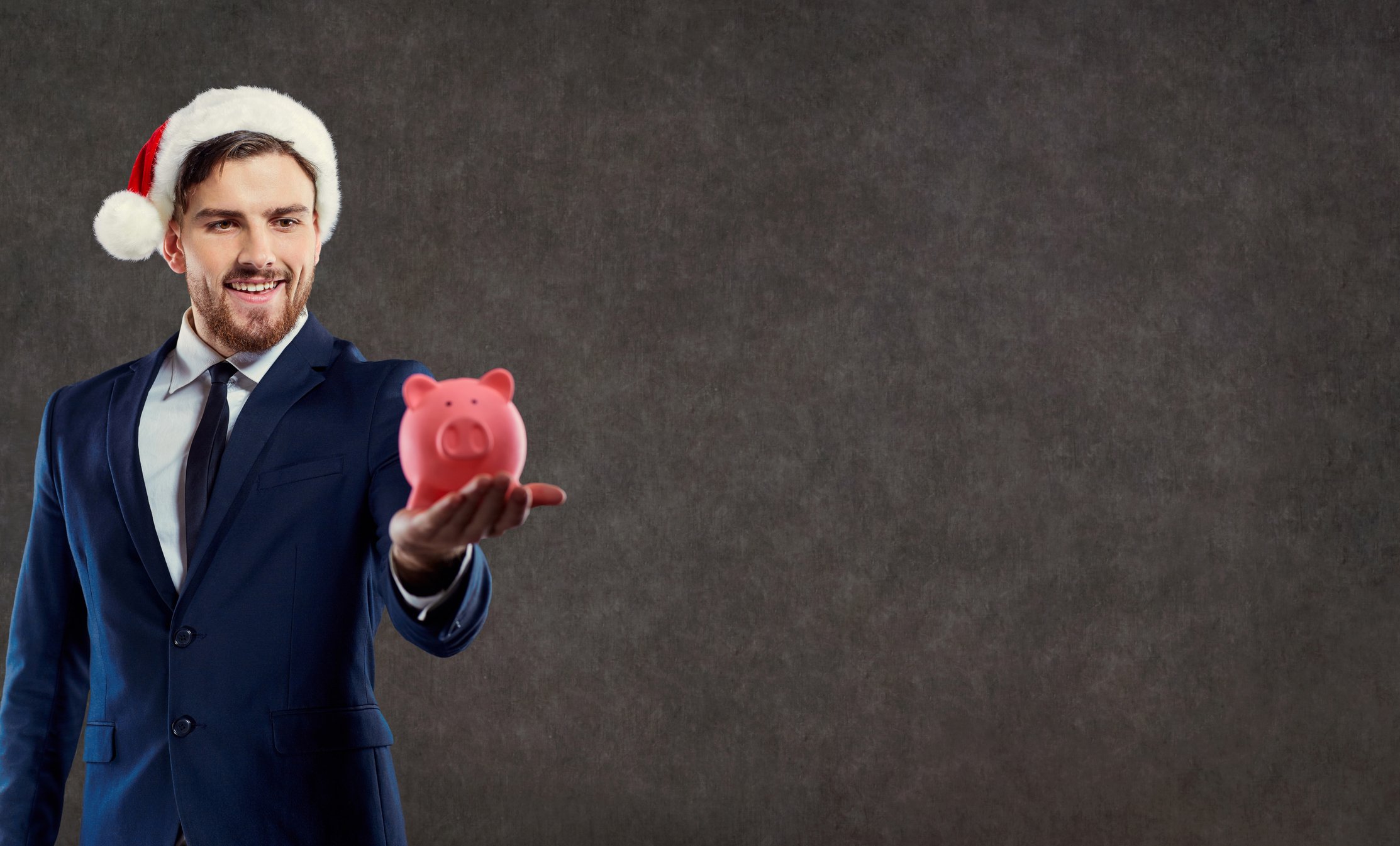 A businessman in a Santa hat holds a piggybank.