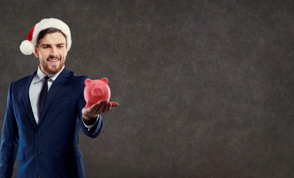 A businessman in a Santa hat holds a piggybank.