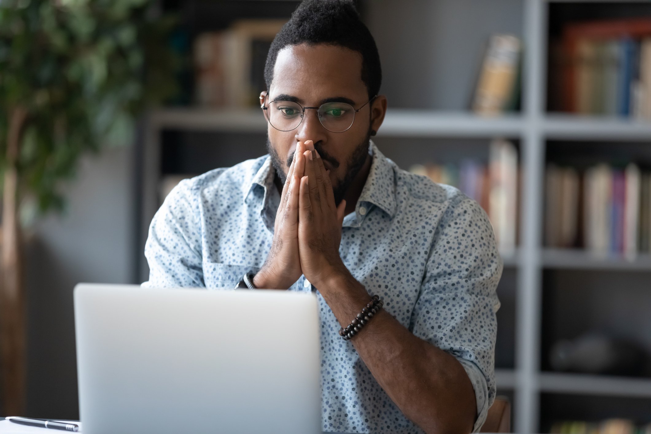 Man with surprised look, hands to his face, as he looks at computer screen