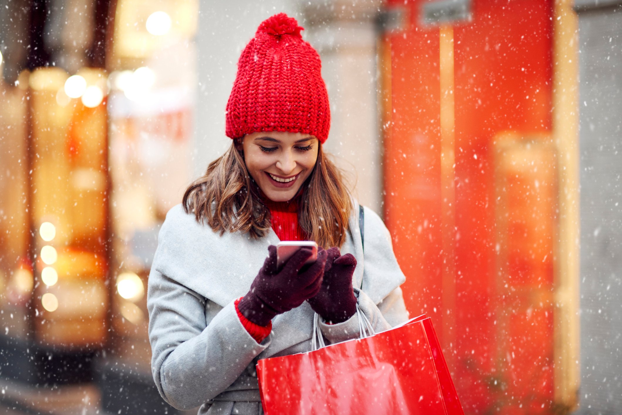 Smiling woman with shopping bags looking at phone in snow