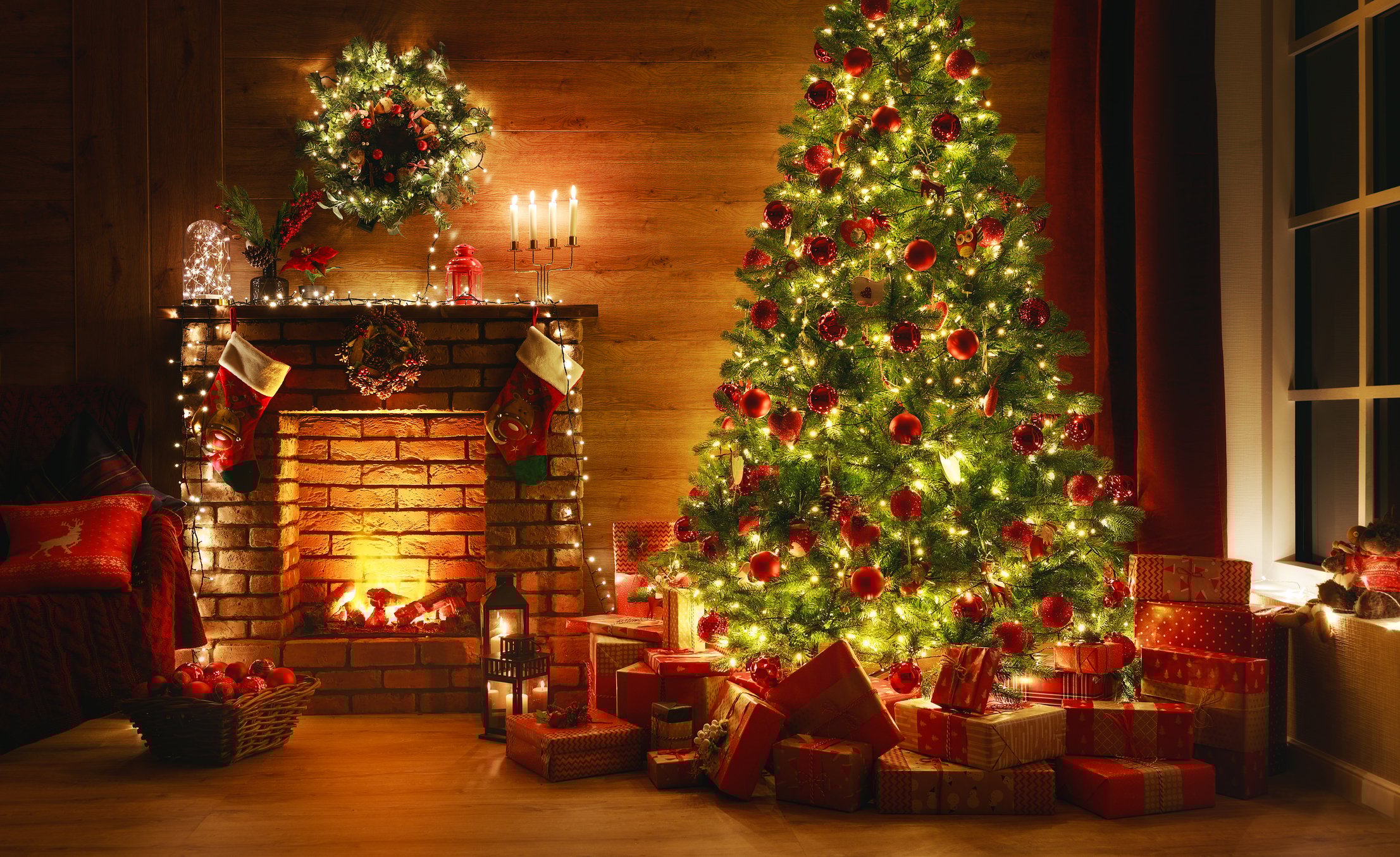 A living room decorated for Christmas, with a fireplace, wreath, Christmas tree and presents