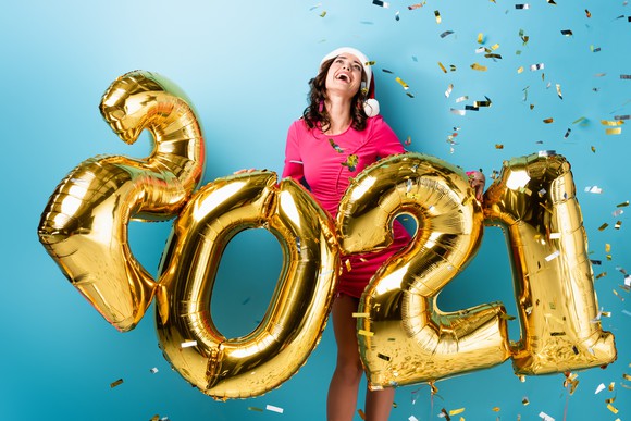 A woman celebrating the new year with 2021 balloons and confetti in the air.