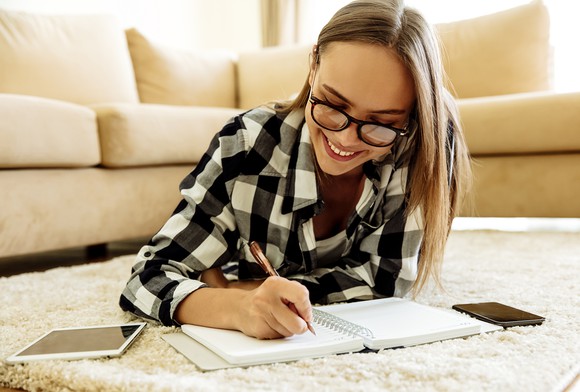 Woman looking at tablet and taking notes in notebook