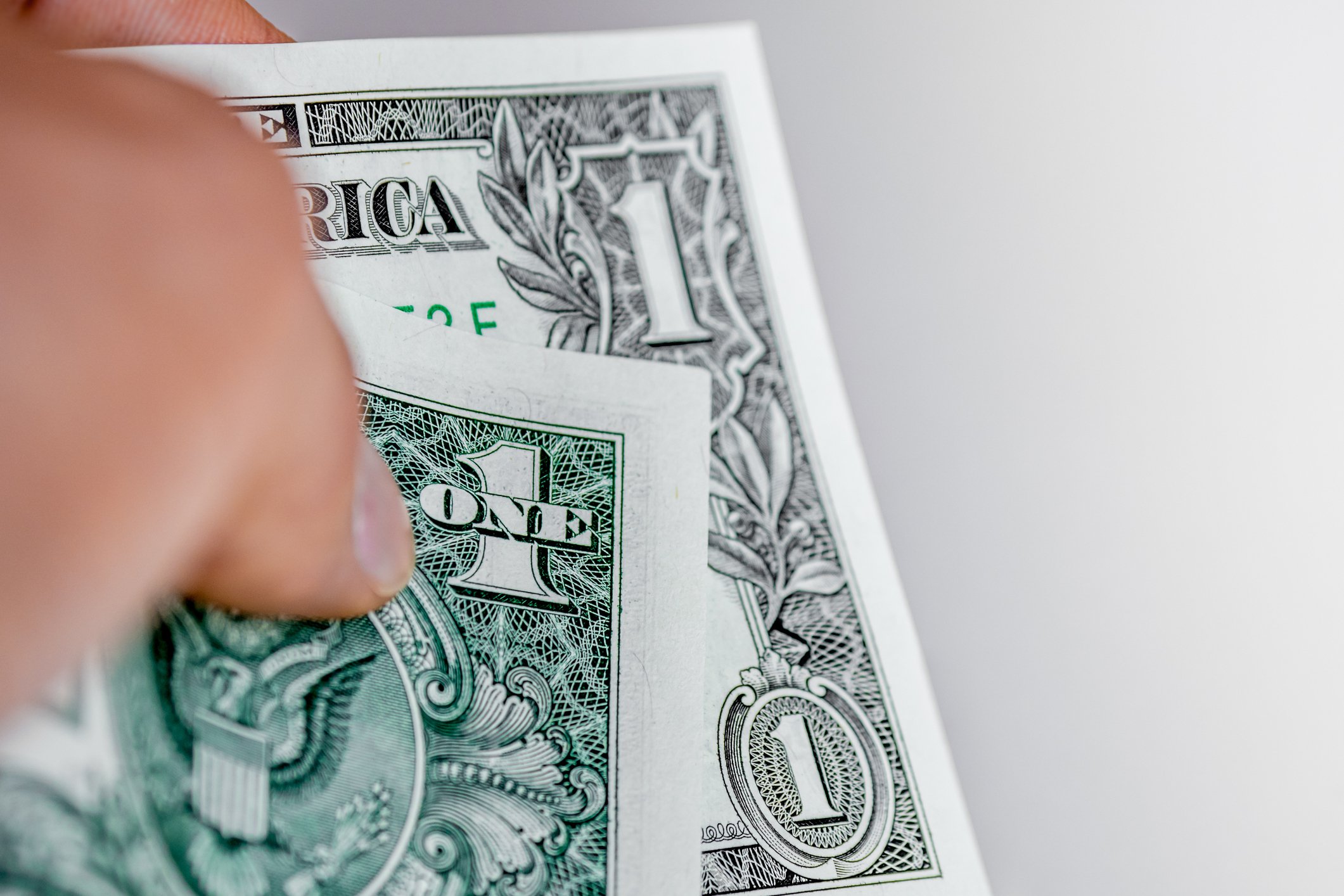 Part of a hand holding a folded dollar bill.