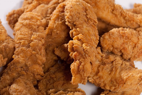 Fried chicken fingers sit on a plate.