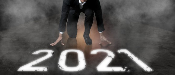 A businessman kneels down at the number 2021 as if to start a sprint race.