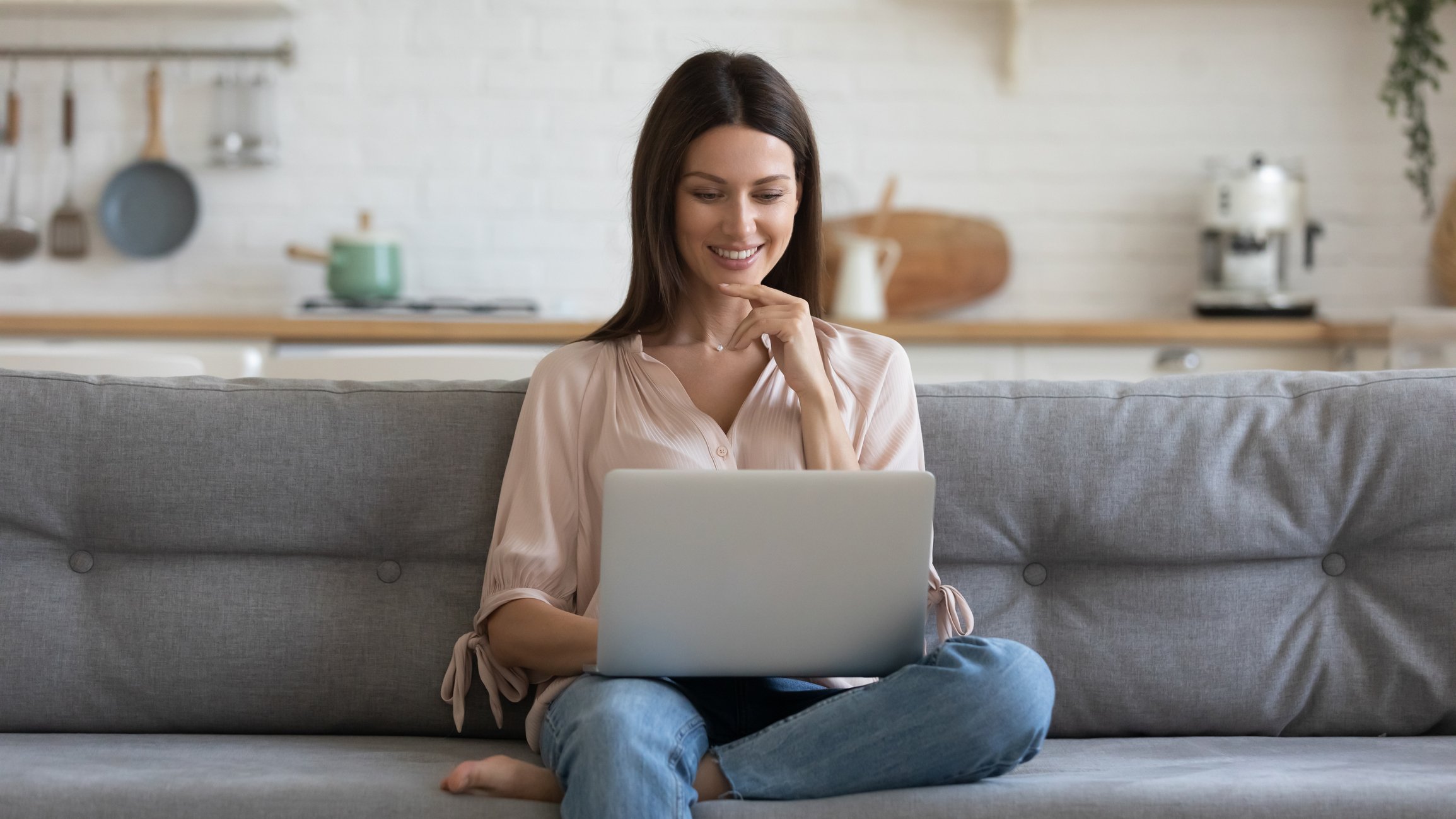 Lady seated on a sofa, smiling while using laptop