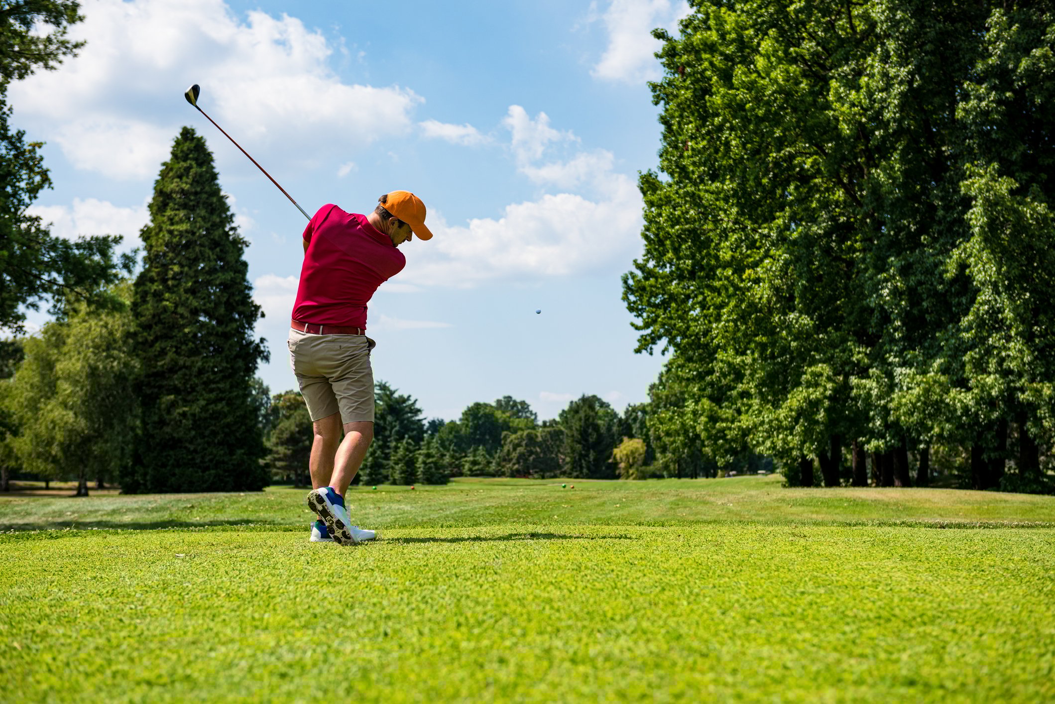 A golfer hits a shot off a tee on a course viewed from the back. 