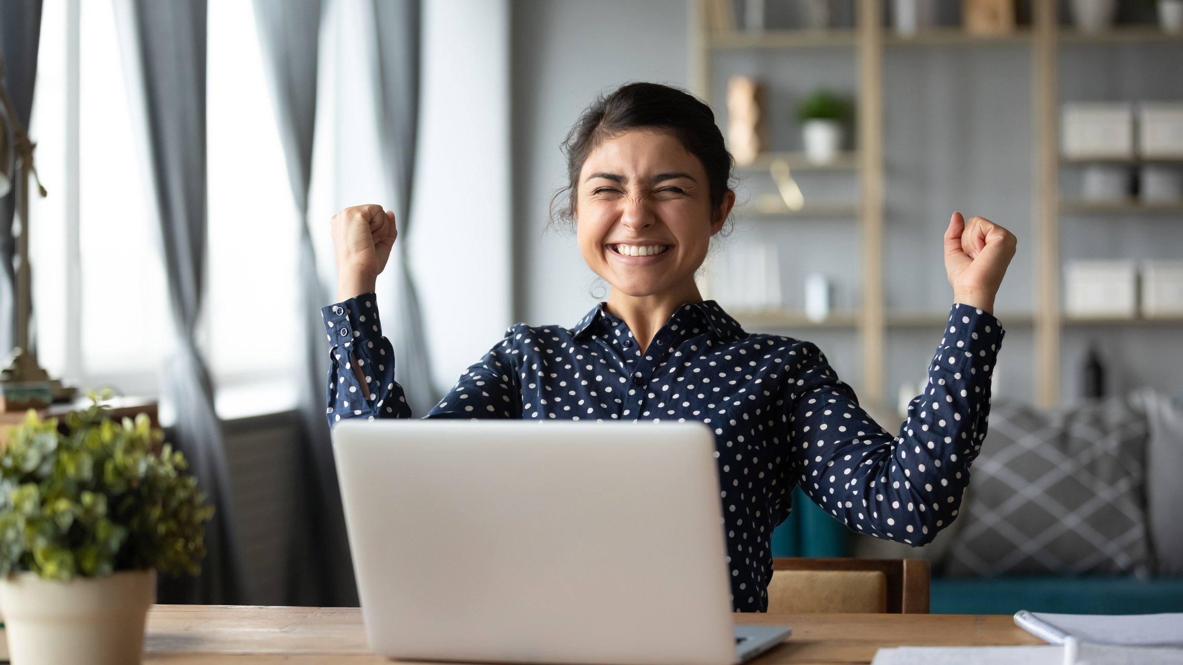 A woman celebrates while sitting behind a laptop.