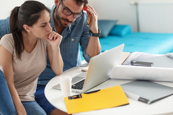 A couple looking at a laptop with papers spread across a desk.