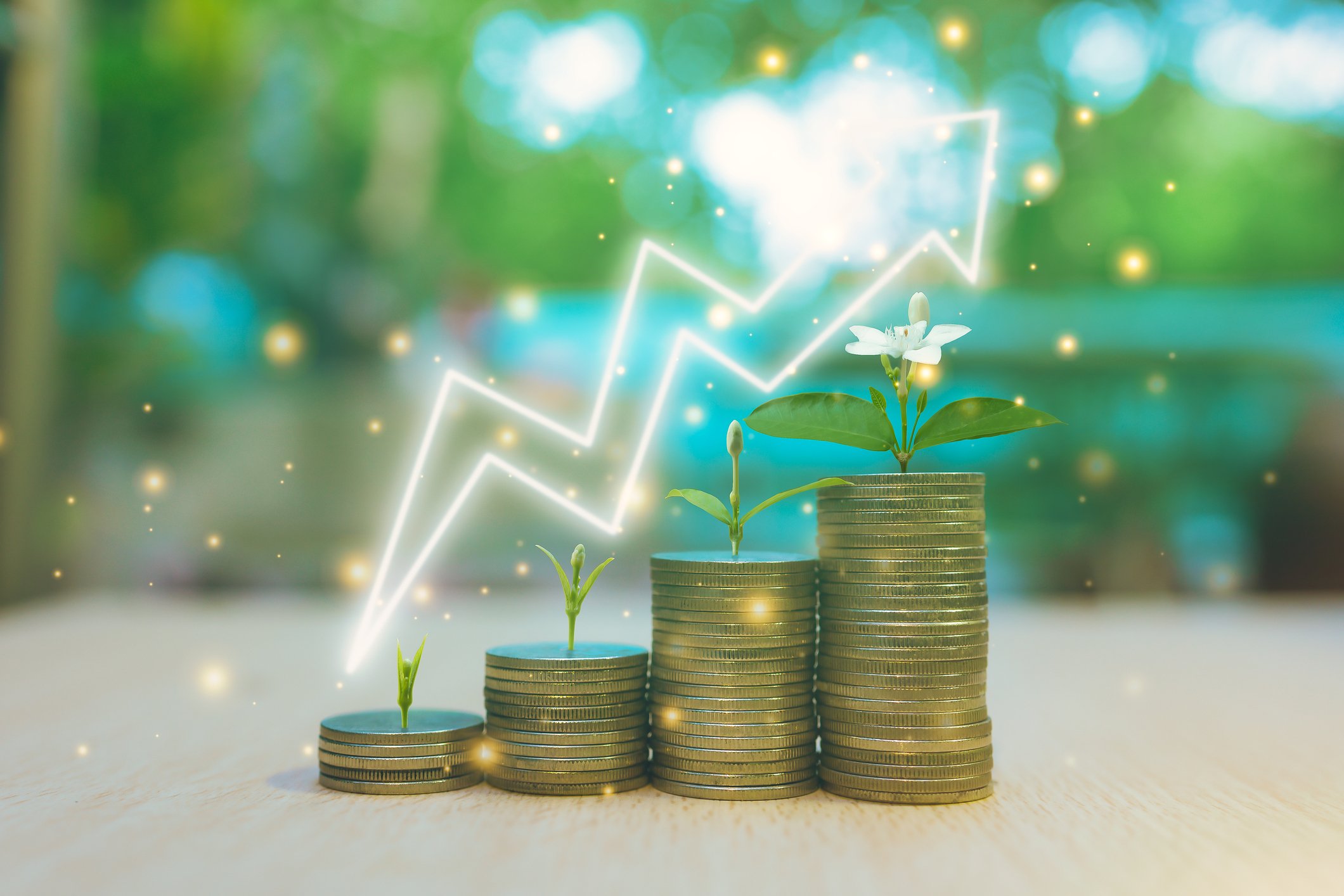 Stacks of coins with plants growing on top are shown on a table witha glowing arrow pointing upward.