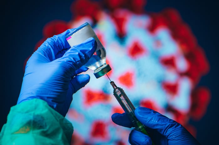 A gloved healthcare worker uses a syringe to draw vaccine from a vial.