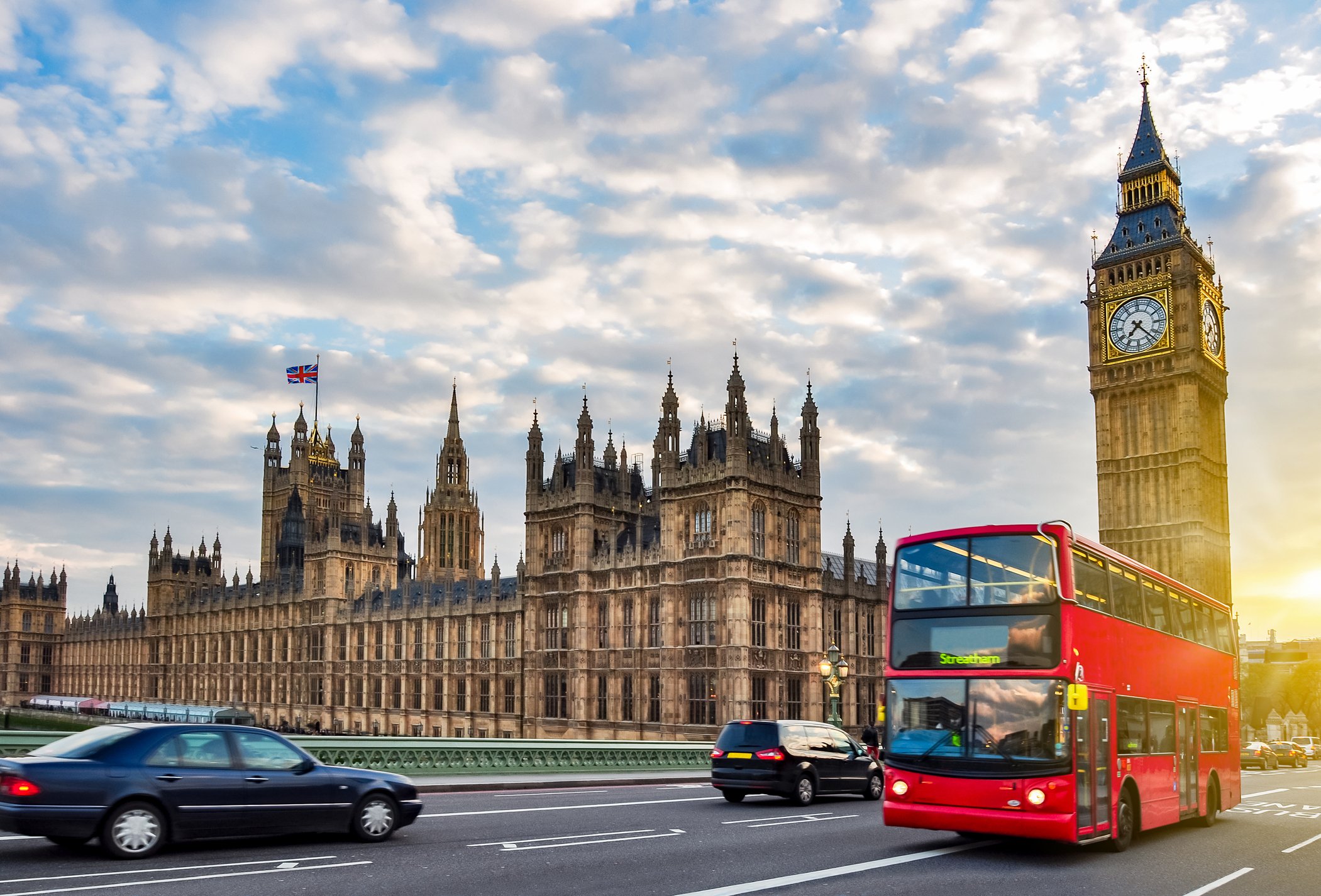 Ben Ben and the Houses of Parliament, major tourist attractions, under a partly cloudy sky, with a double decker bus in the foreground.