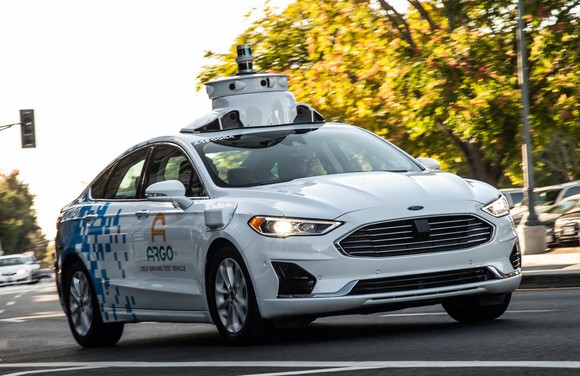 A white Ford Fusion sedan with Argo AI logos and visible self-driving sensor hardware