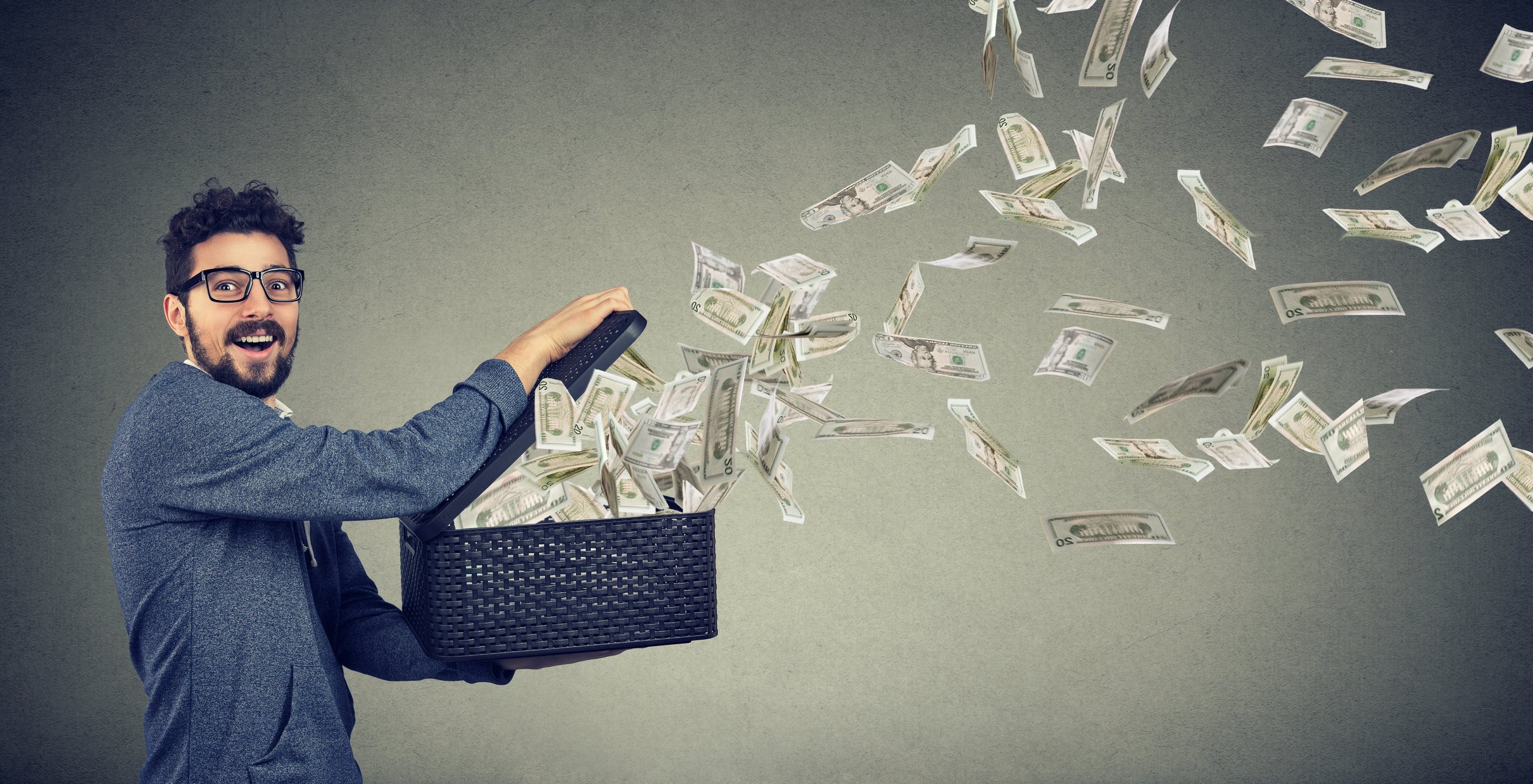 Dollar bills flying out of a basket held open by a man.
