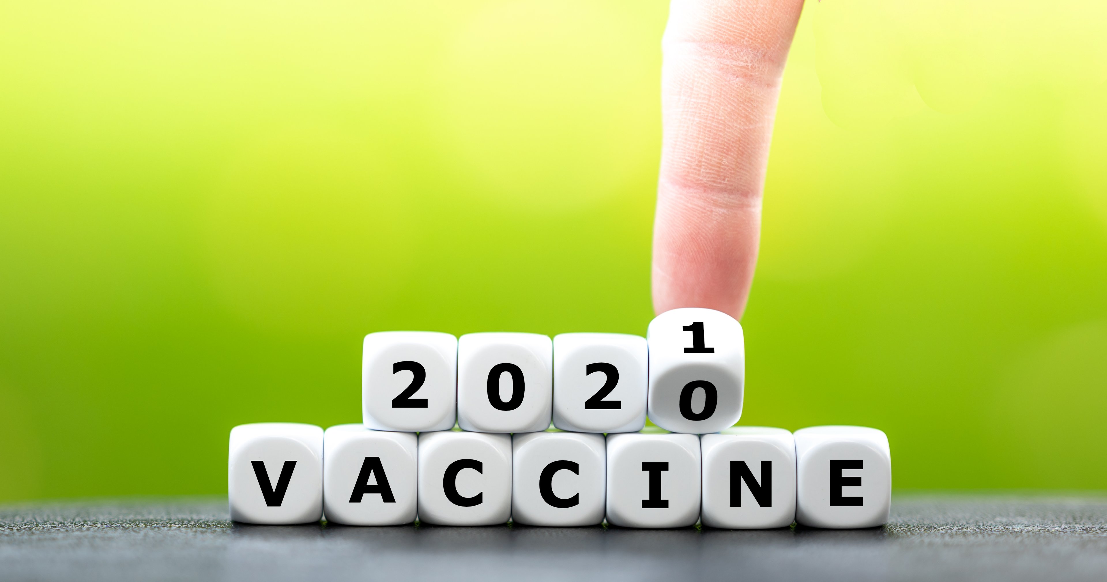 A man's finger turns blocks reading "2020 vaccine" to "2021."