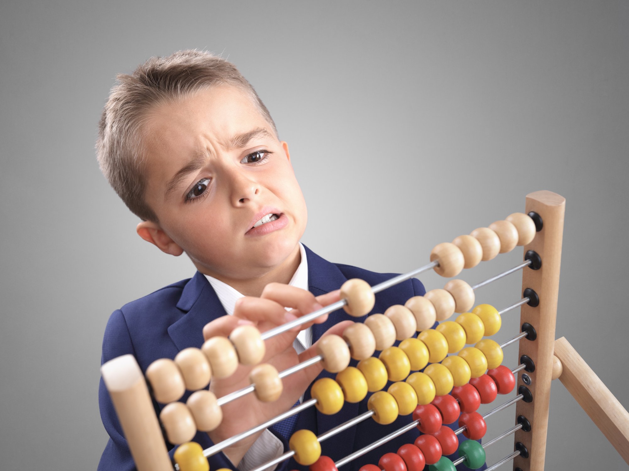 A young boy in a suit struggles to use an abacus.