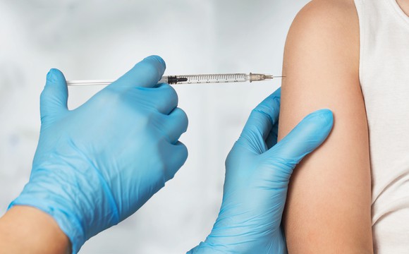 A gloved hand injects a vaccine into a patient's arm.