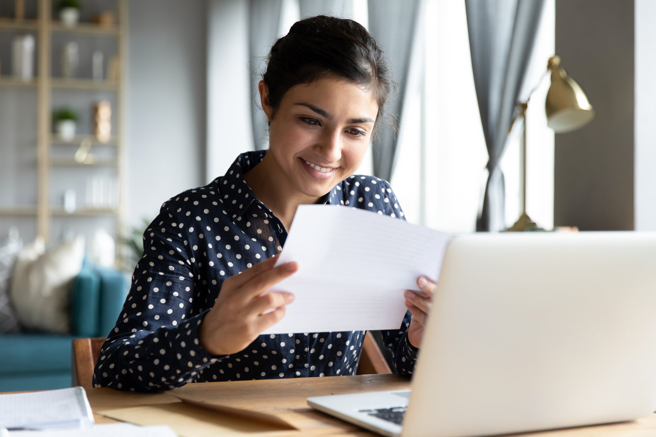 A smiling woman at a desk reads a document. 