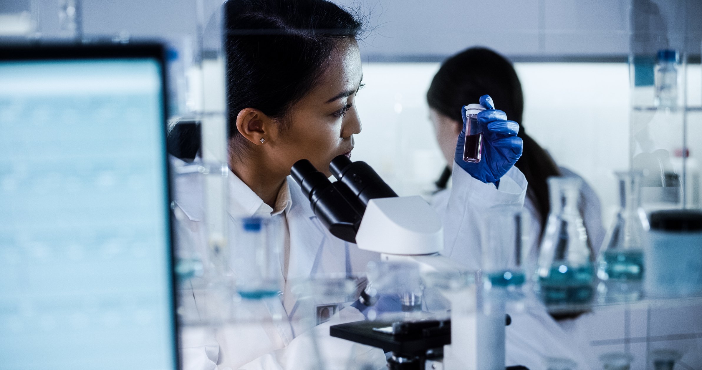 A scientist examines a vial in front of a microscope.