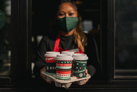 A Starbucks employee wears a facemask while serving coffee contained in holiday cups.