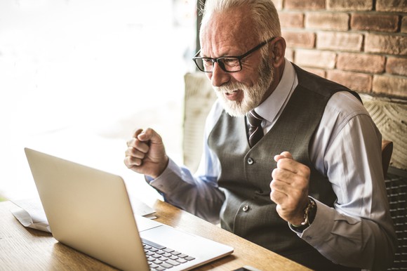 Smiling older man responding to good news on his laptop.